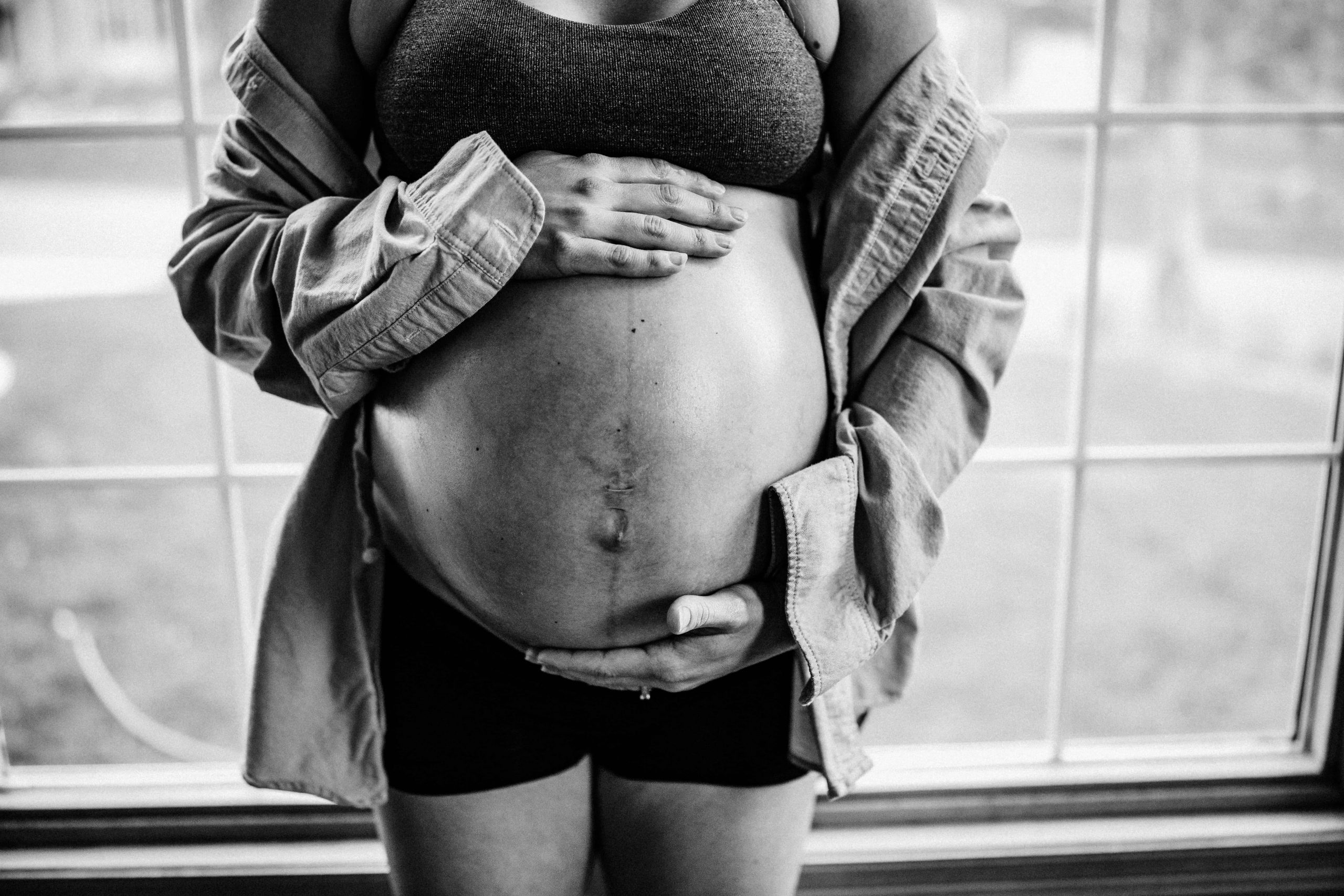 Mama holds her belly in black and white image at her intimate at-home maternity session