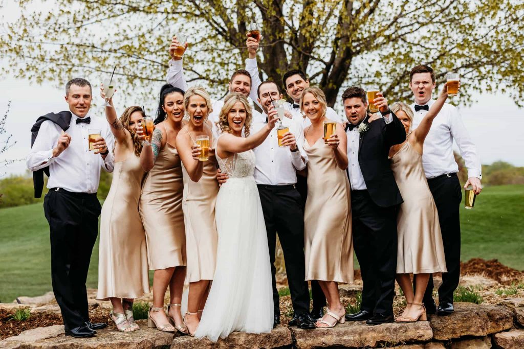 Couple and their wedding party celebrate with a drink all huddled together outside of their Hazeltine National Golf Club wedding