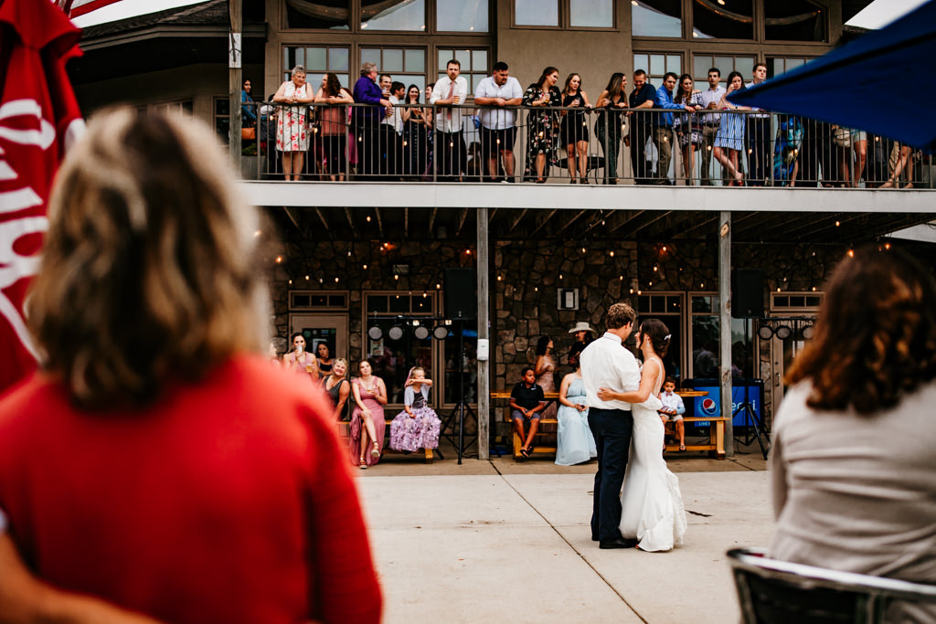 A couple dances together during their first dance outdoors as guests look on from patio and upper balcony