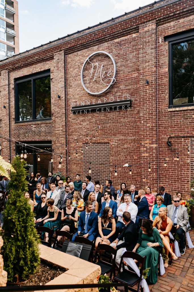 Wedding guests sit in rows of chairs outside of Minneapolis Event Center Wedding in the outdoor courtyard.