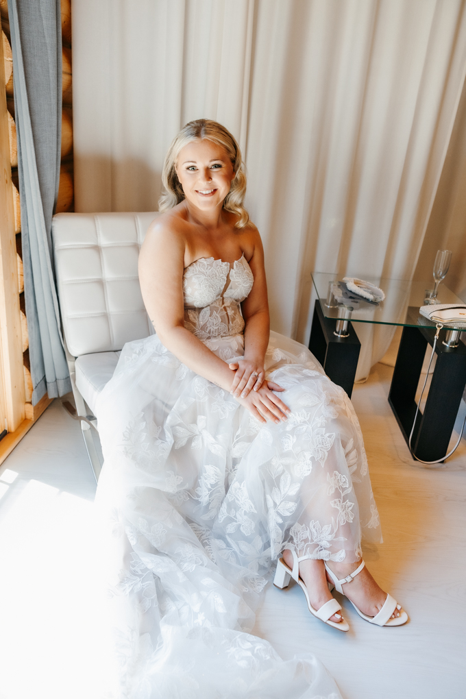 Bride sits on a white plush chair and smiles at the camera before her Northern oaks events wedding