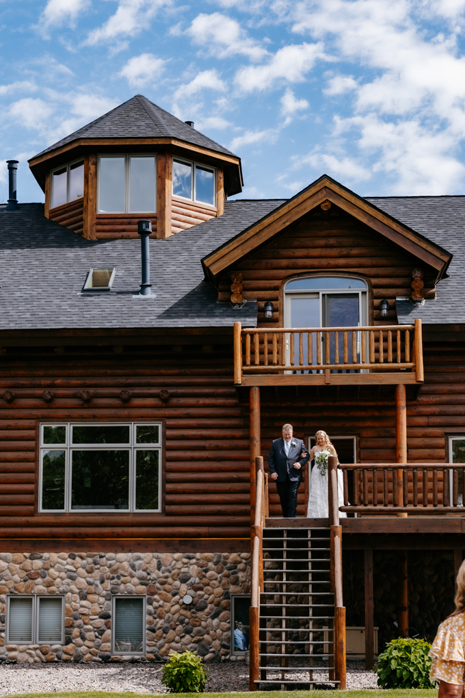 Bride and her dad come down the stairs of the log cabin house at Northern oaks event wedding