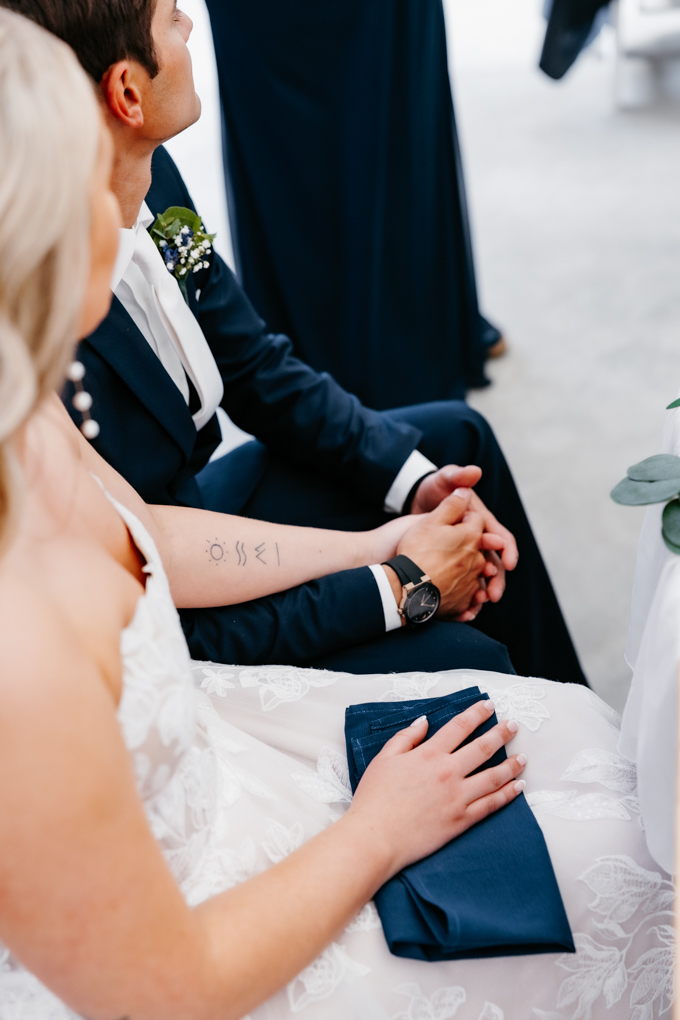 Bride and groom hold hands during the speech portion of their 10-hour wedding timeline