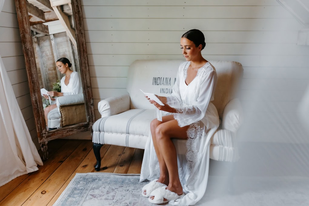 Bride reads a letter from her husband in her robe in the bridal suite at her Gathered Oaks wedding