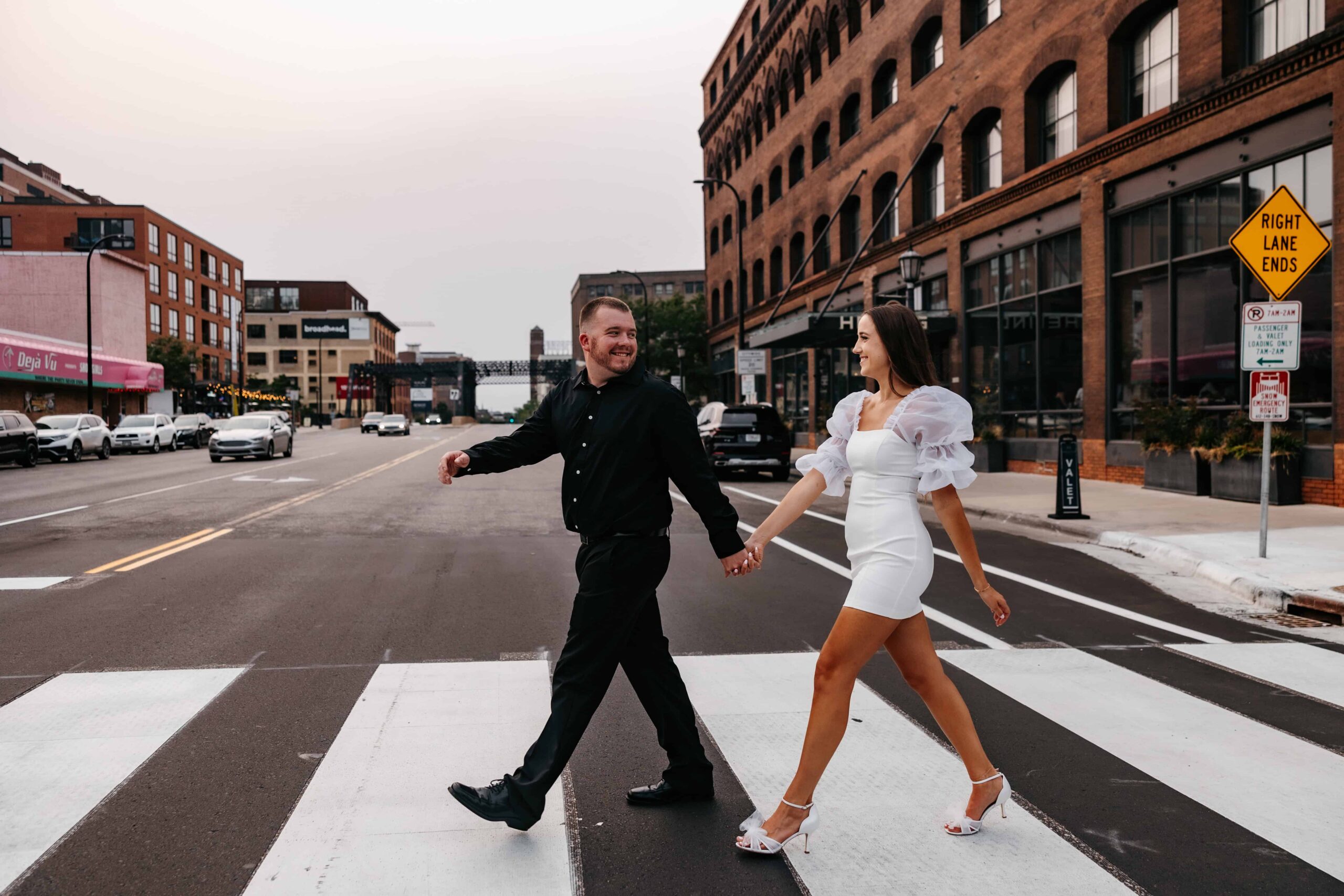 A bride and groom walk down the street hand in hand durin their minneapolis engagement photo shoot