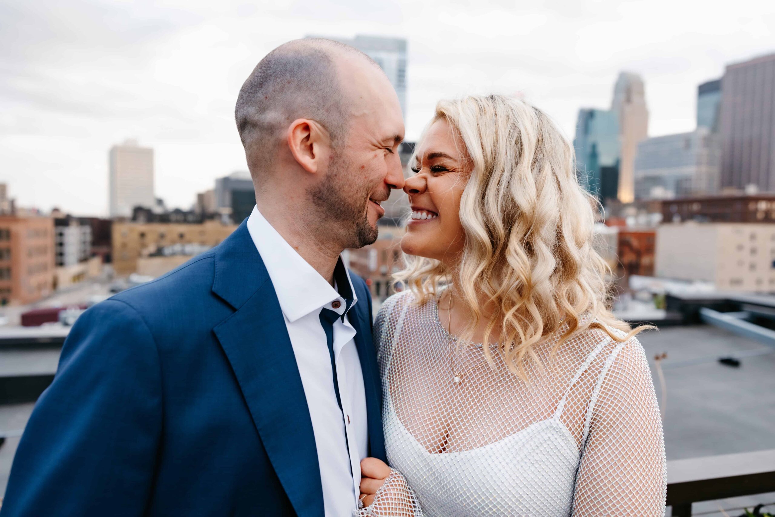 a man and woman smiling and touching noses in front of minneapolis skyline at engagement photography session