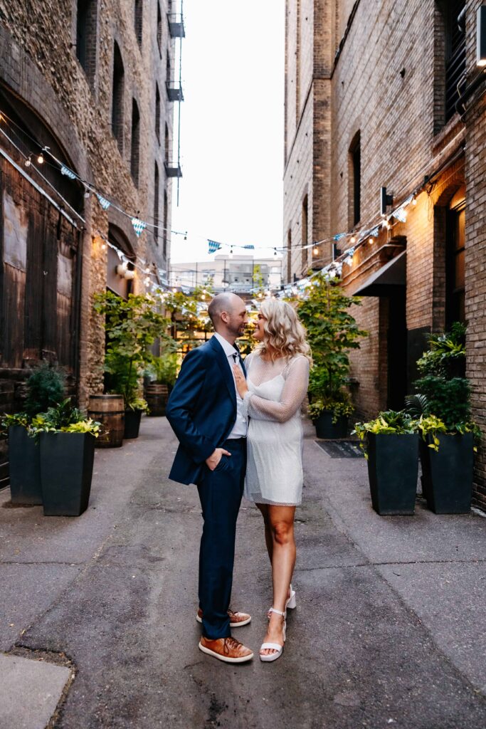 a man and woman standing in a alley smiling at each other during minneapolis engagement photography session