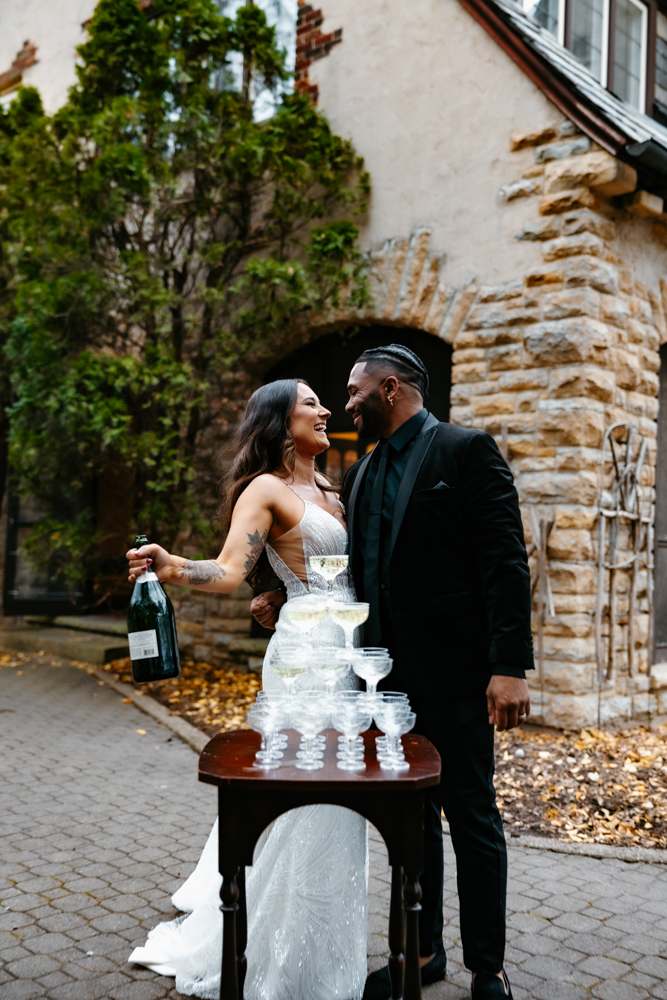 bride and groom stand together with champagne tower and kiss at their rochester mn wedding venue