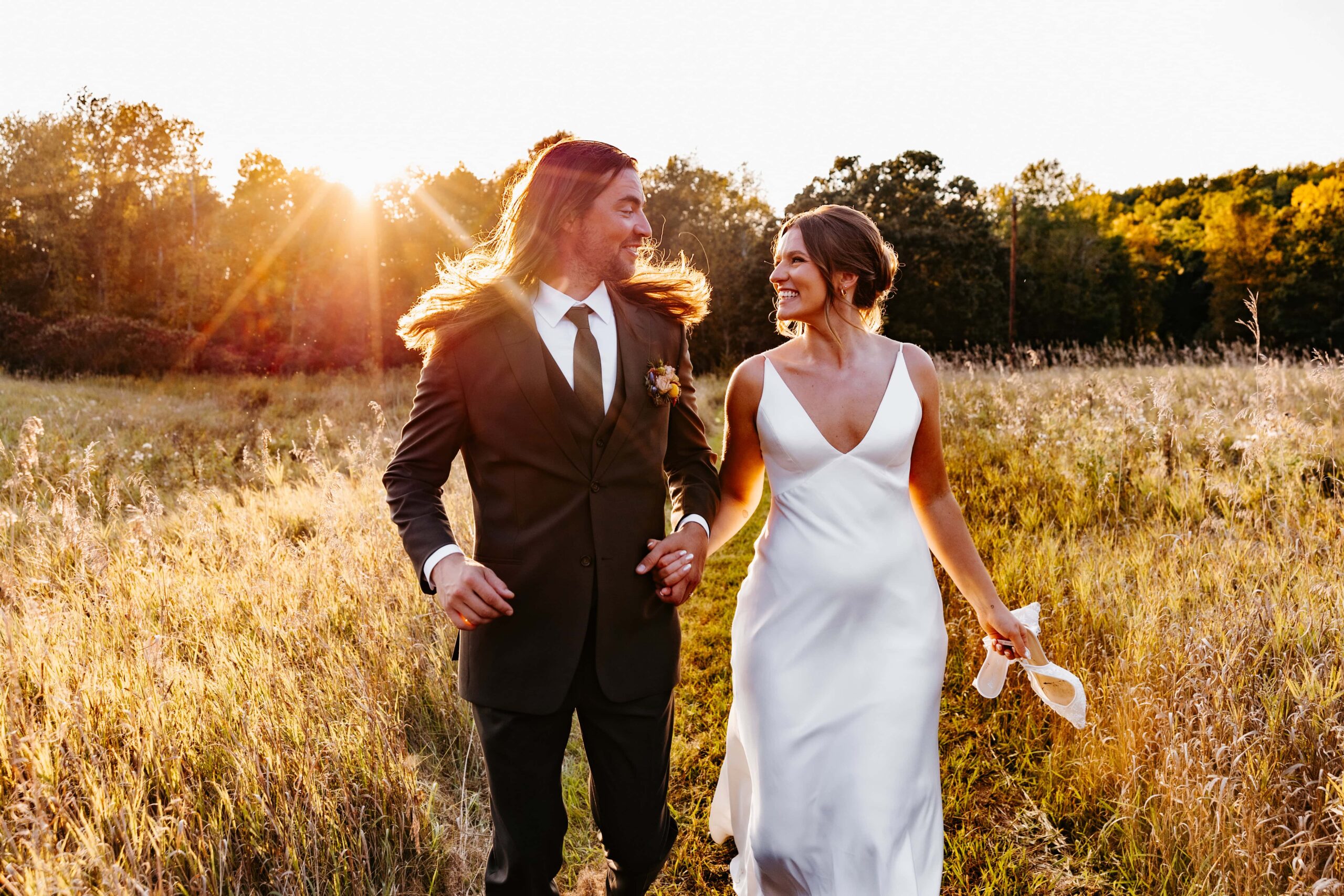 Bride & groom smile and laugh as they run through the field at their st. cloud wedding at avon folk school