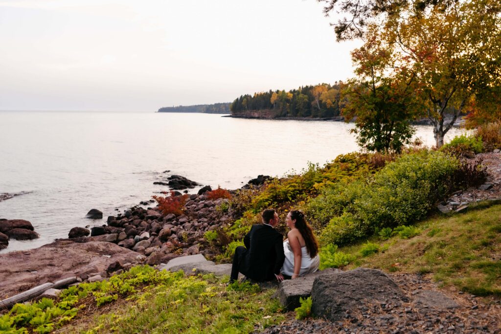 Bride and groom sit along a rocky cliff overlooking lake superior for a private moment at their wedding at Grand Superior Lodge