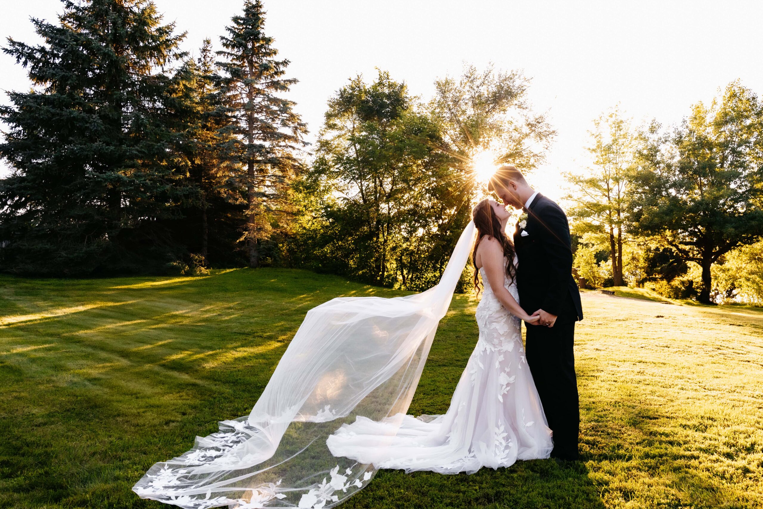 Bride and groom kiss with the brides veil blowing in the breeze as during their time for golden hour photos in minnesota