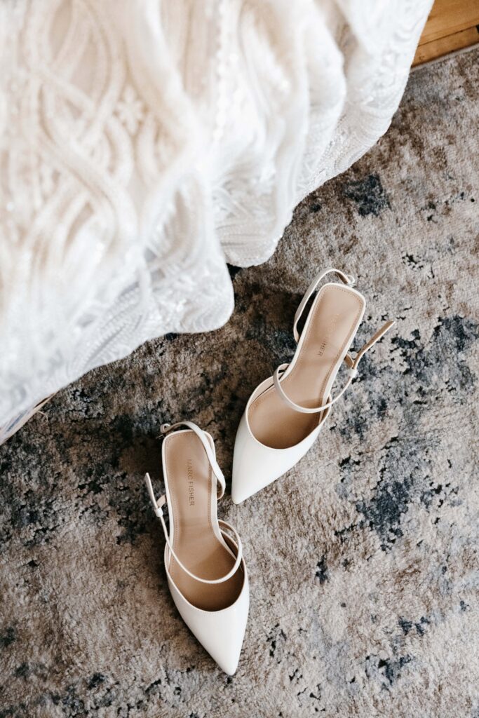 A pair of white pointed toe wedding shoes sit on the floor of the bridal suite at Jerome Event Center wedding venue