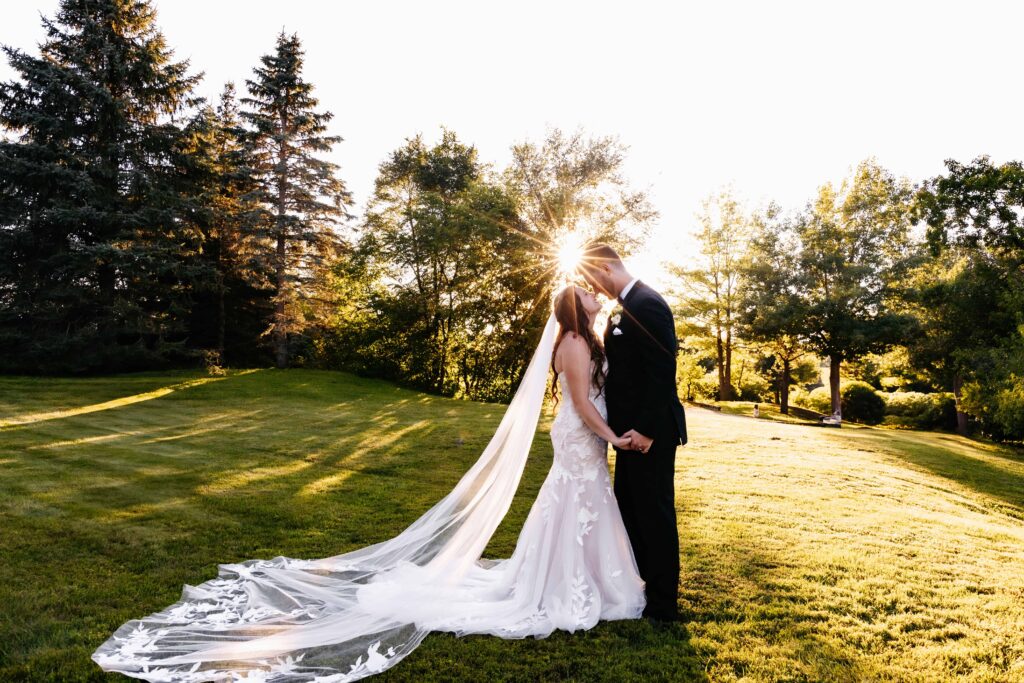 Bride in a white dress with long white veil kisses her husband in a black suit at her gardens of castle rock wedding at sunset